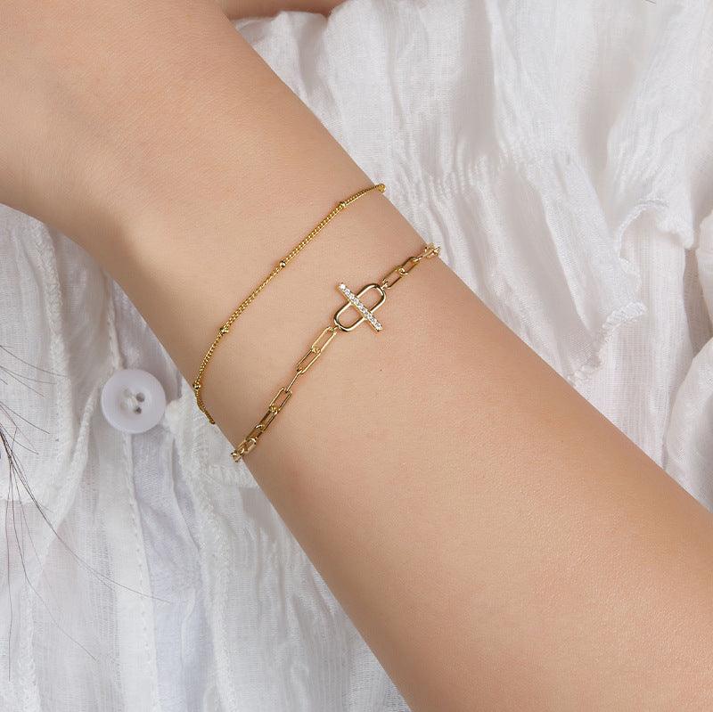 Model wearing a stylish gold chain bracelet with a minimalist clasp design, paired elegantly with a delicate chain bracelet.