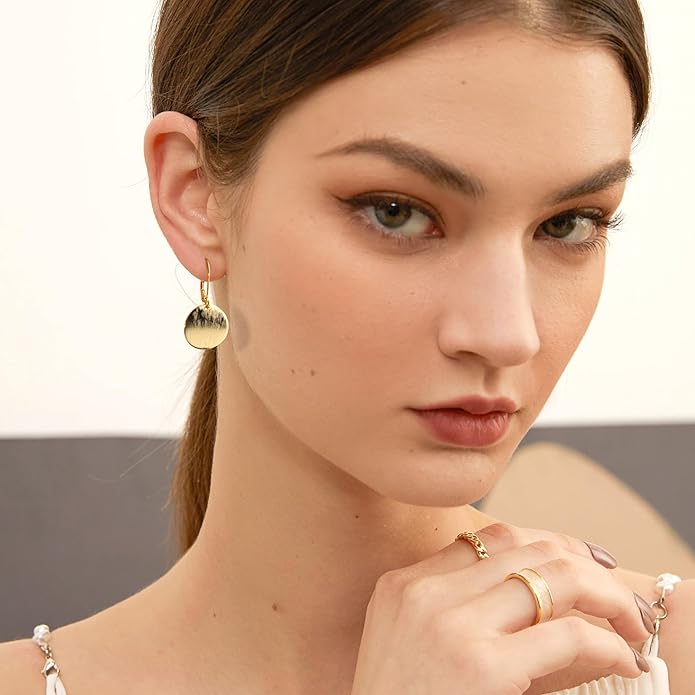 Model wearing elegant gold drop earrings and minimalist rings, showcasing a sophisticated jewelry style.