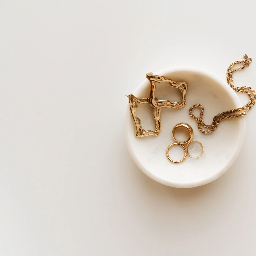 Elegant gold jewelry pieces including rings, a necklace, and abstract-shaped earrings displayed on a marble dish.