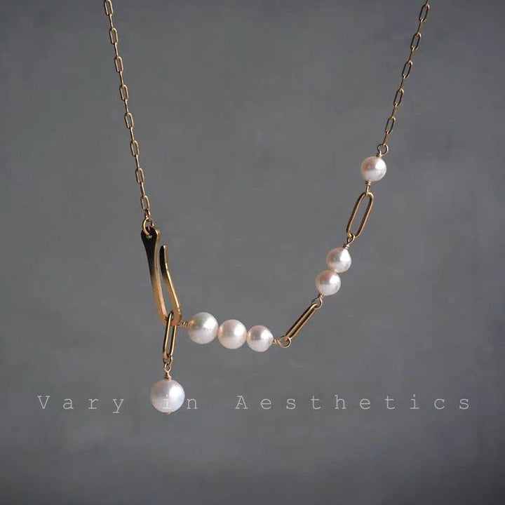 Modern asymmetrical gold chain necklace with white pearls and a dangling pearl charm.