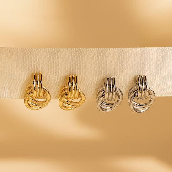 A set of interlocking hoop earrings in gold and silver tones displayed on a beige ribbon against a warm background, showcasing their polished and elegant design.