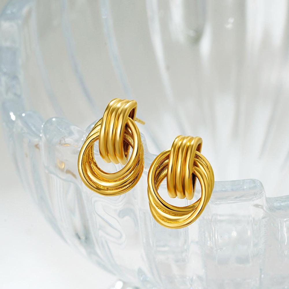 A pair of gold-tone interlocking hoop earrings displayed on a translucent glass surface, highlighting their polished and elegant design.