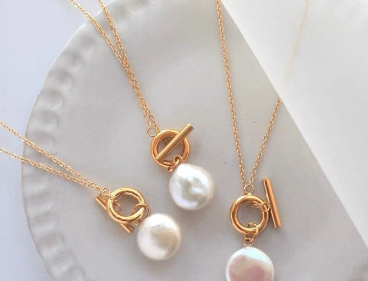 Set of gold chain necklaces with toggle clasps and white pearl pendants displayed on a white plate.