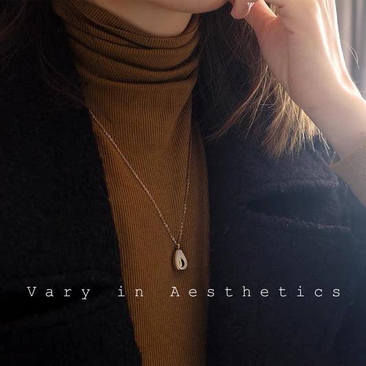 Gold teardrop pendant necklace worn over a brown turtleneck and black coat.