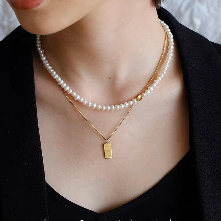 Elegant layered necklace with a pearl choker and a gold bar pendant worn over a black outfit.