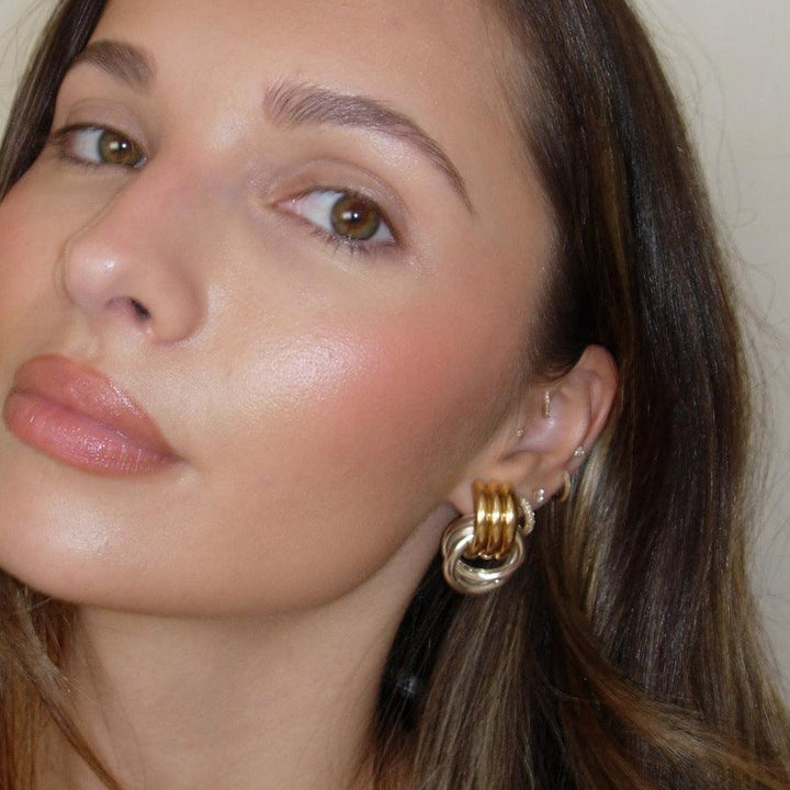 A close-up of a woman wearing dual-tone interlocking hoop earrings in gold and silver, styled with natural makeup, highlighting the earrings' elegant design.