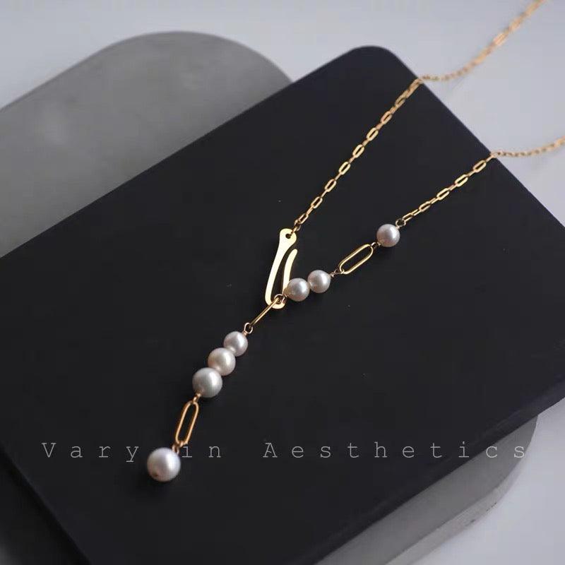 Elegant gold chain necklace with white pearls and a drop design on a black background.