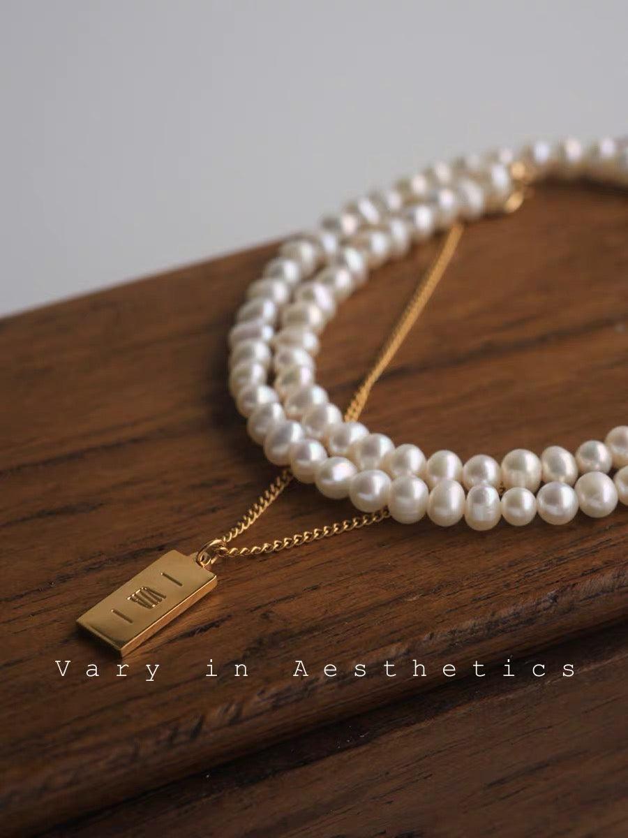 Double-layer pearl necklace with a gold bar pendant displayed on a wooden surface.