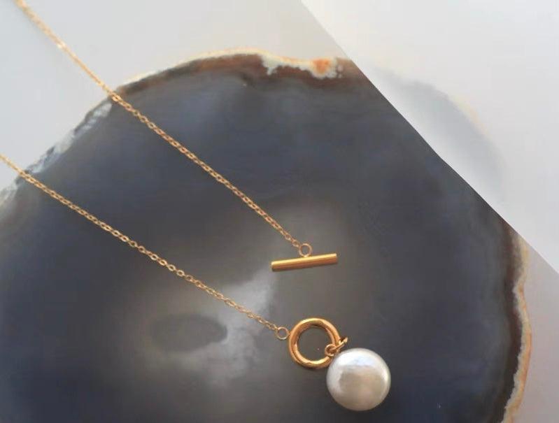 Gold chain necklace with a toggle clasp and a single white pearl pendant displayed on a dark agate slice.